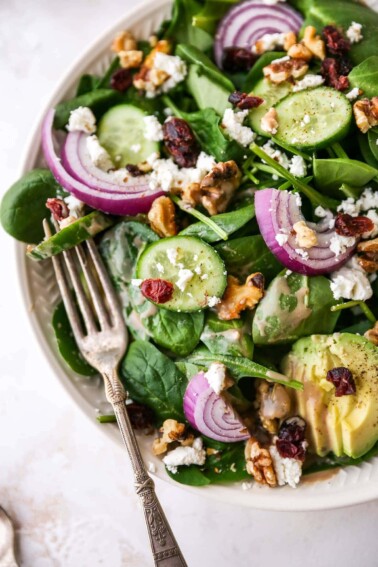 Plated spinach salad topped with avocado, goat cheese, cranberries, walnuts, onion and a drizzle of creamy balsamic dressing.