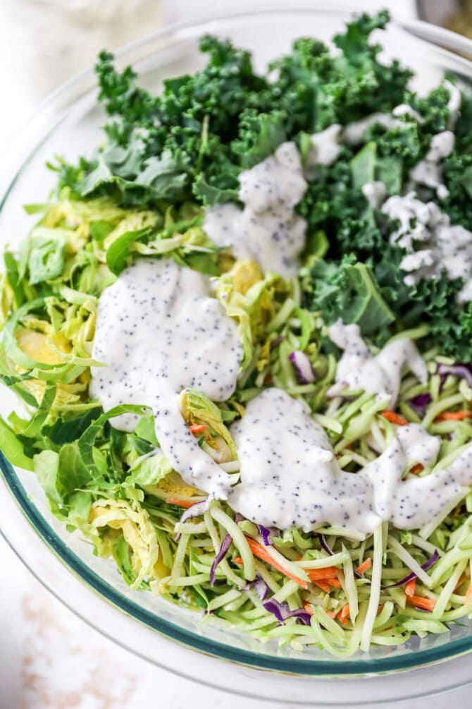 Mixing bowl with shredded brussels, slaw and kale topped with poppyseed dressing.