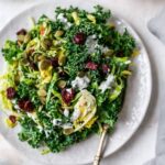 Plate and fork with sweet kale salad topped with poppyseed dressing, cranberries and pepitas.