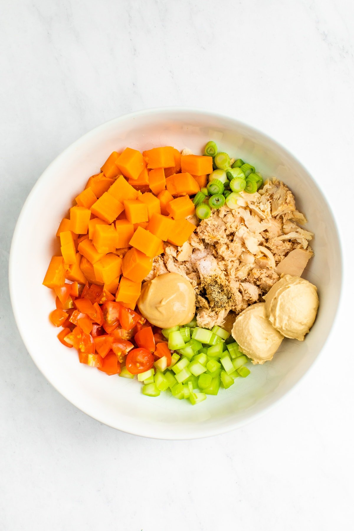 Bowl with sweet potatoes, green onion, tuna, hummus, spices, mustard, celery and tomatoes.