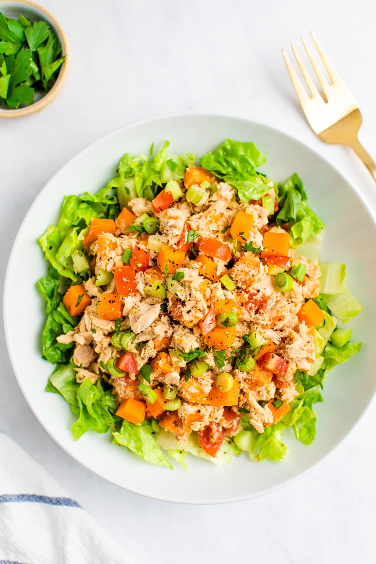 Sweet potato tuna salad served on a bed of lettuce. A fork and a bowl of parsley are beside the salad.
