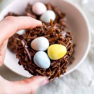 Hand holding a chocolate coconut nest with candy eggs in the middle.