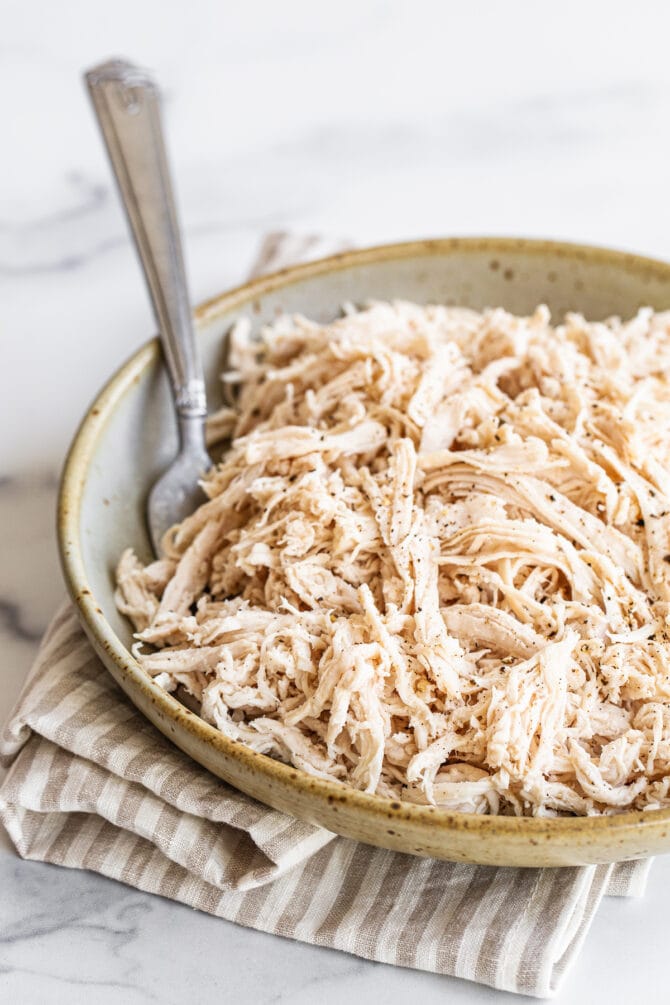 Shredded chicken in a shallow bowl. A fork rests inside the bowl.