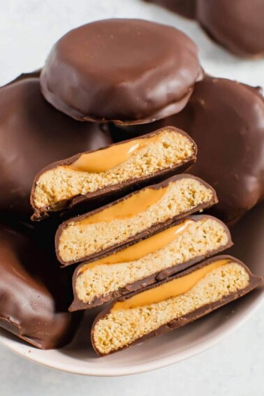 Homemade Tagalongs cut in half so you can see the cookie and peanut butter. These cookies are in a bowl of other chocolate covered Tagalongs.