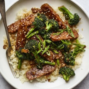 Bowl with rice topped with teriyaki tempeh and broccoli and sesame seeds. A fork is in the bowl.