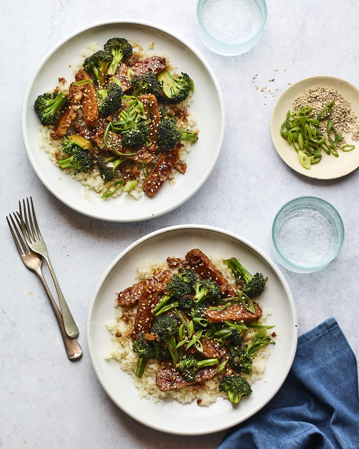 Two plates of teriyaki tempeh and broccoli served over rice.