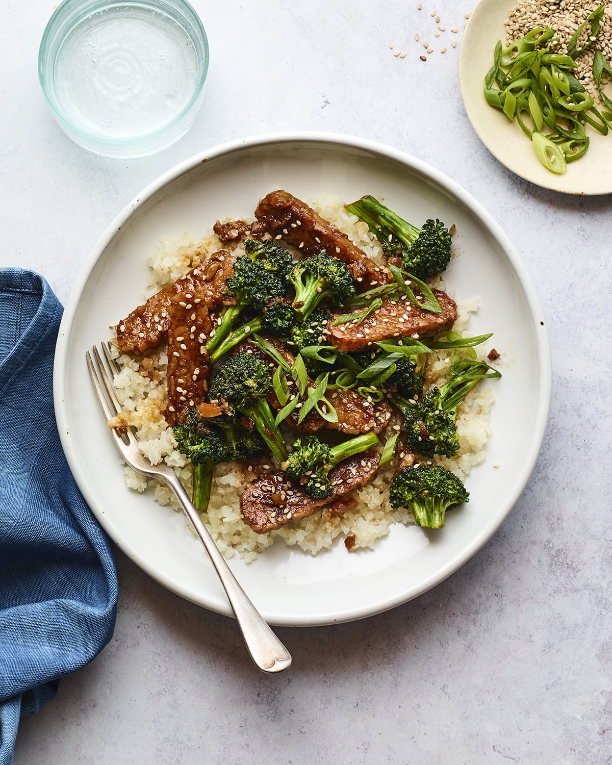 Bowl with rice topped with teriyaki tempeh and broccoli and sesame seeds. A fork is in the bowl.