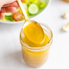 Spoon with a spoonful of apple cider dressing from a mason jar.