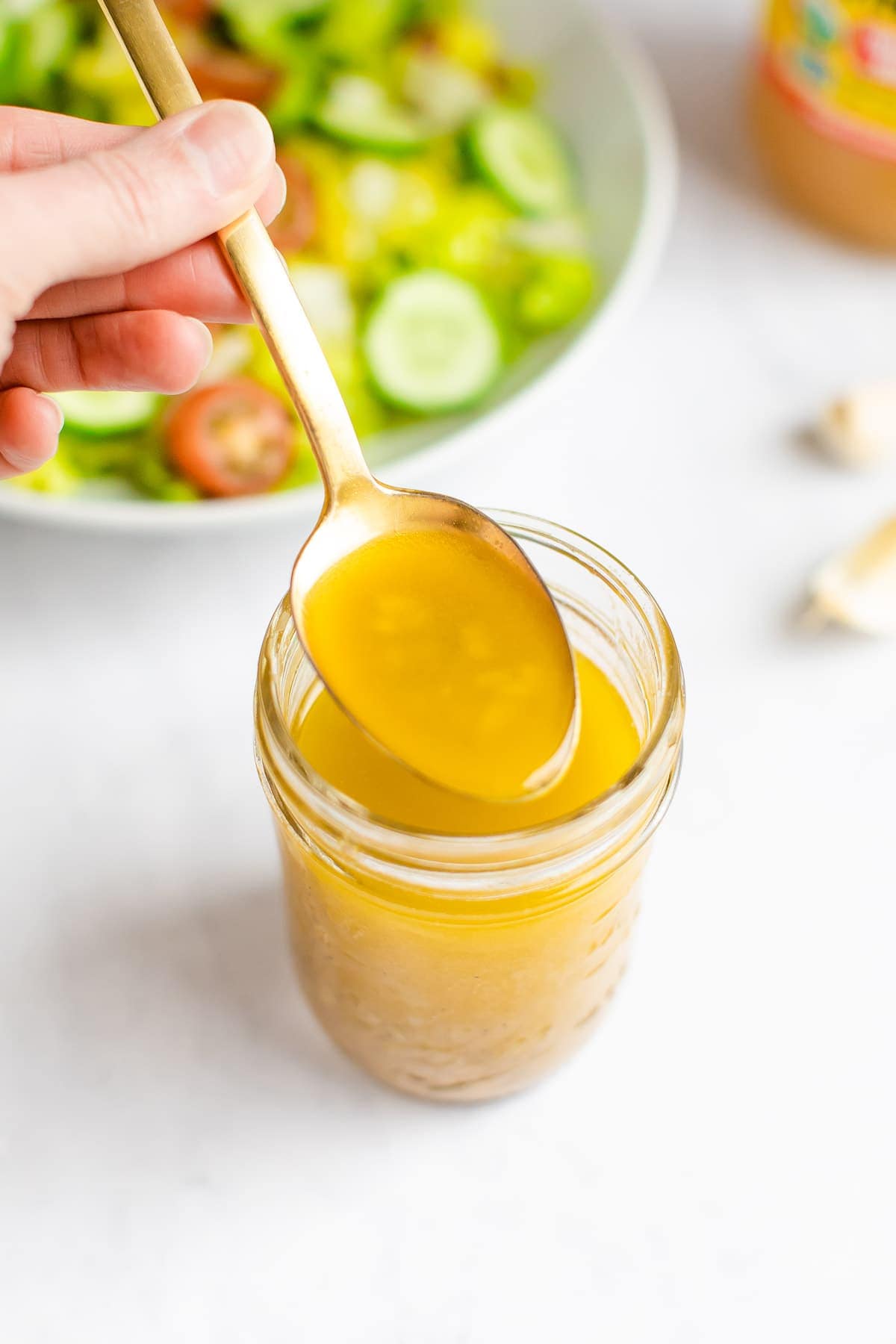 Spoon with a spoonful of apple cider dressing from a mason jar.