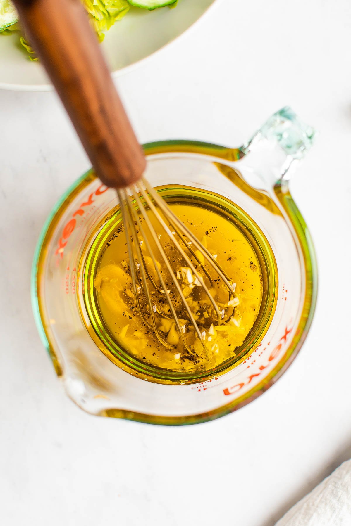 Glass measuring cup with a whisk and ingredients to make apple cider dressing before being whisked.