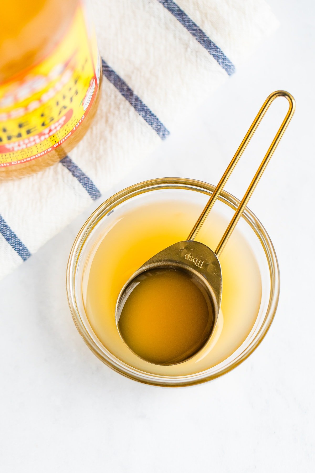 Apple cider vinegar in a small glass bowl with gold tablespoon.