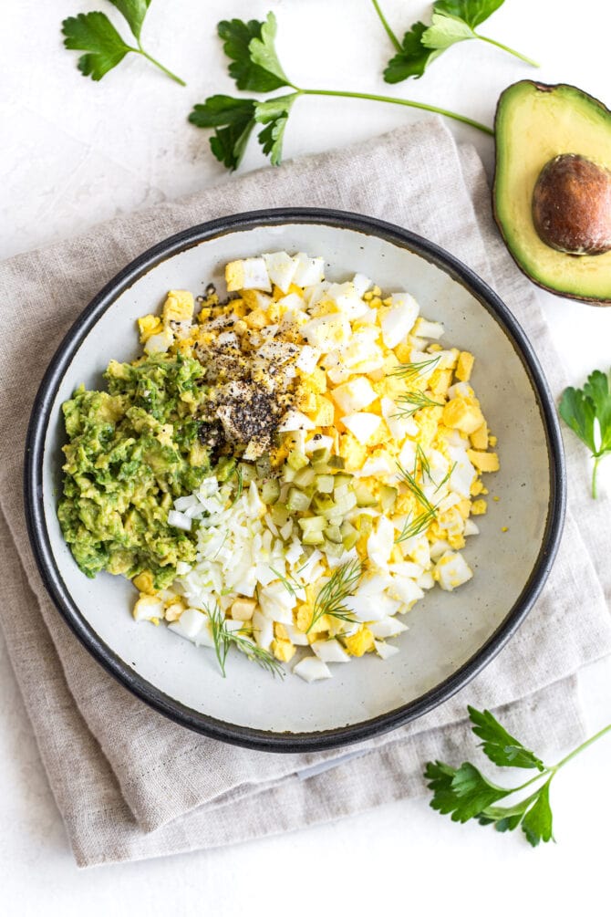 Bowl with mashed avocado onion, eggs and herbs.