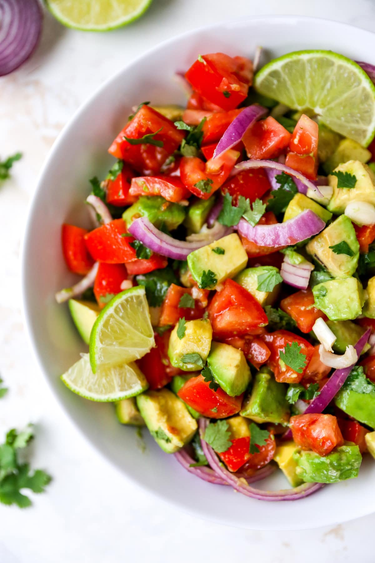 Serving bowl with avocado and tomato salad garnished with lime and cilantro.