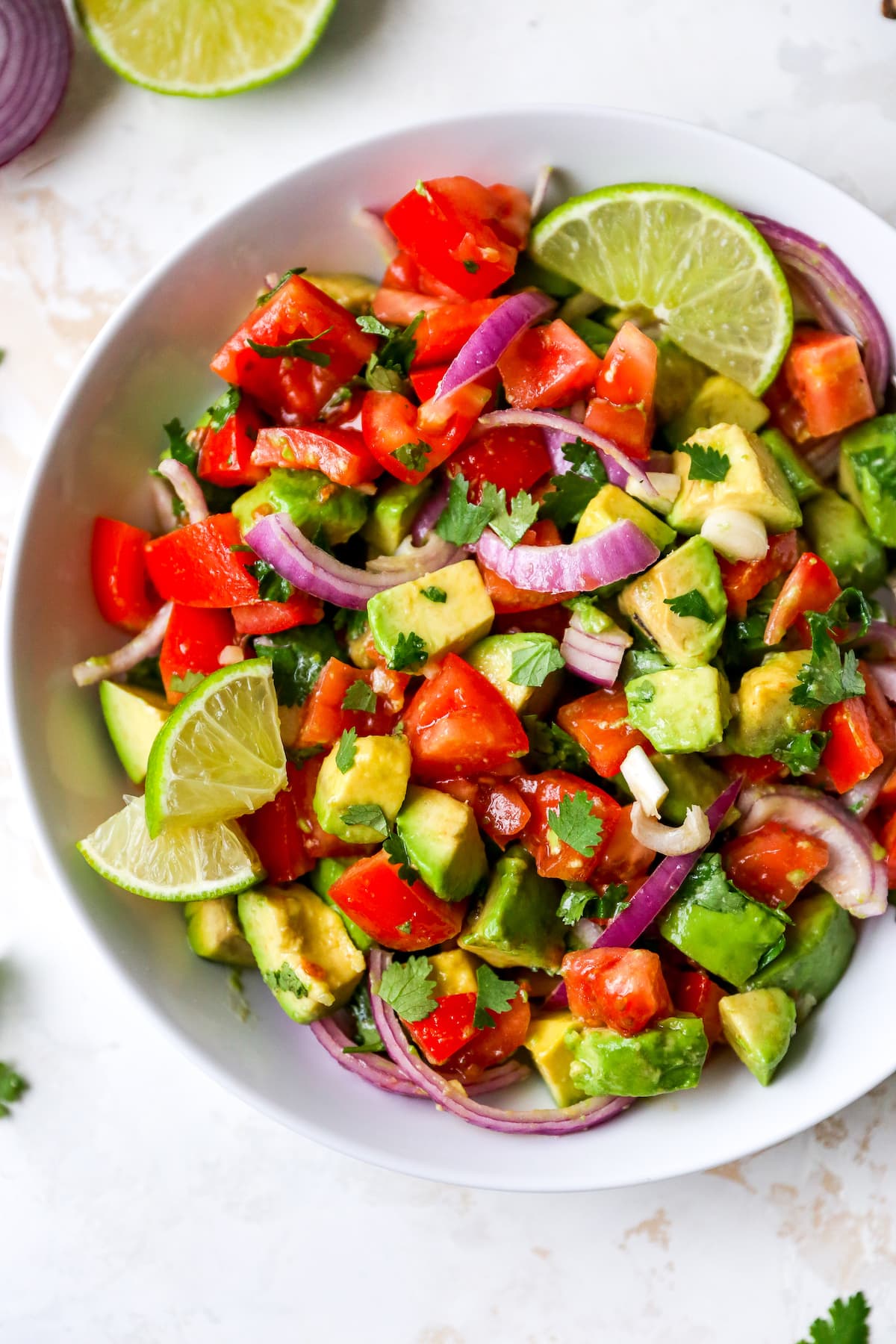 Serving bowl with avocado and tomato salad garnished with lime and cilantro.