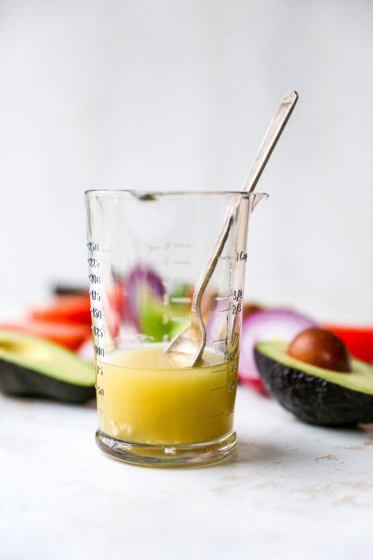 Clear measuring cup with a lime homemade dressing and a spoon.