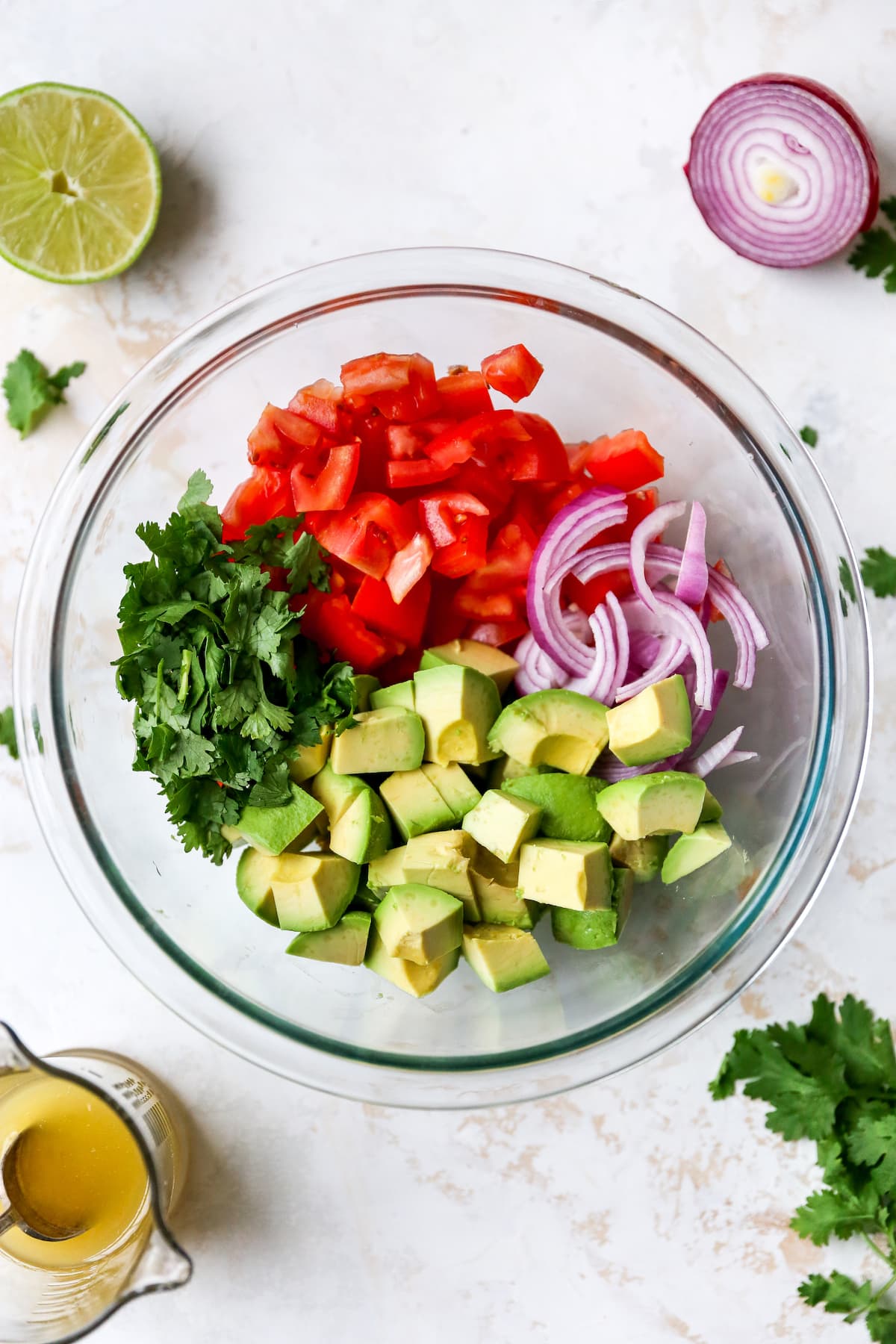 Glass mixing bowl with chopped tomato, red onion, avocado and cilantro.