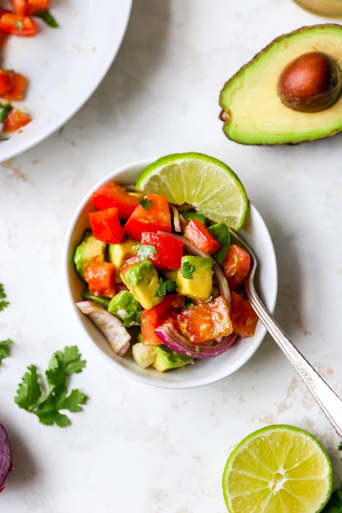 Salad bowl with avocado tomato salad garnished with lime and cilantro. A fork is in the bowl.