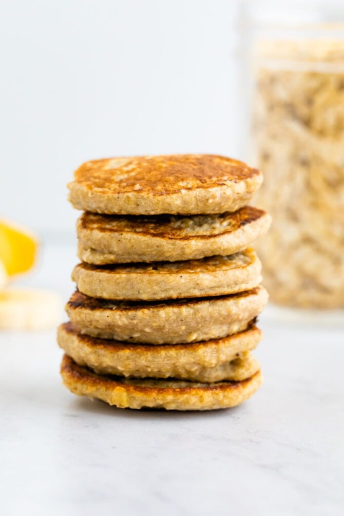 Stack of small pancakes. Banana and oats in the background.