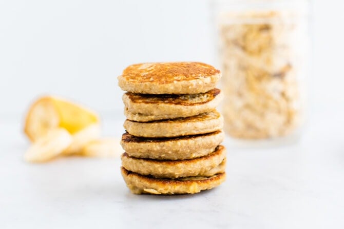 Stack of small pancakes. Banana and oats in the background.