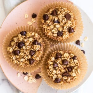 Three chocolate chip baked oatmeal cups on a plate, topped with chocolate chips.