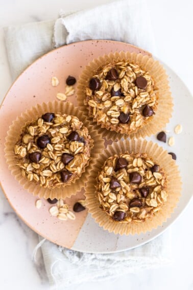 Three chocolate chip baked oatmeal cups on a plate, topped with chocolate chips.