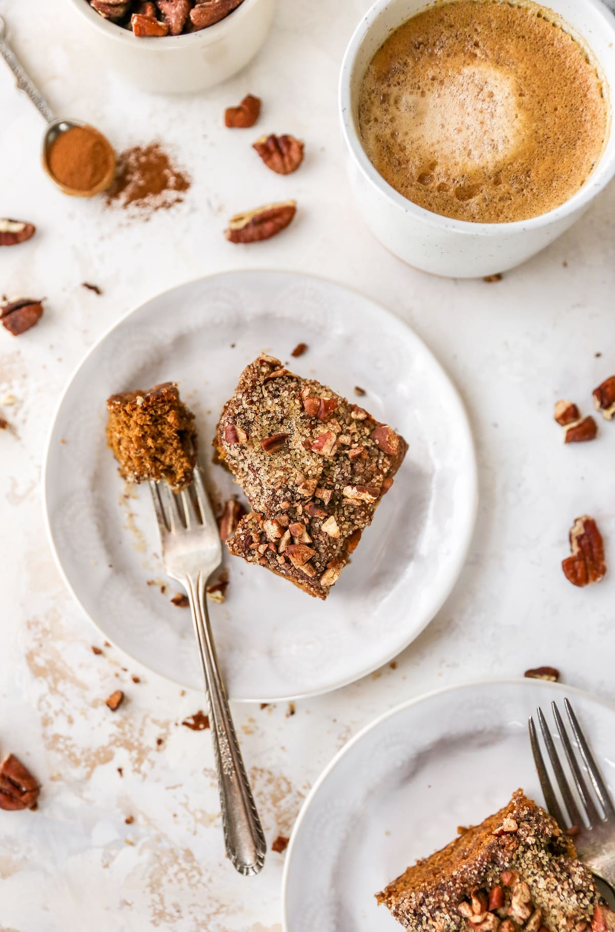 Slices of coffee cake on plates. A fork has taken a bite out of the cake. A latter is beside the plates.