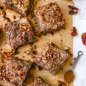 Slices of coffee cake on parchment paper. a teaspoon of cinnamon and bowl fo pecans are on the table too.