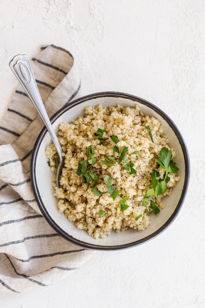 Bowl of quinoa with a serving spoon. Quinoa is topped with pepper and chopped parsely.