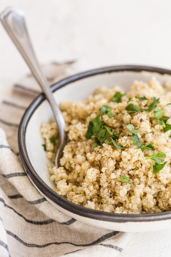 Bowl of quinoa with a serving spoon. Quinoa is topped with pepper and chopped parsely.