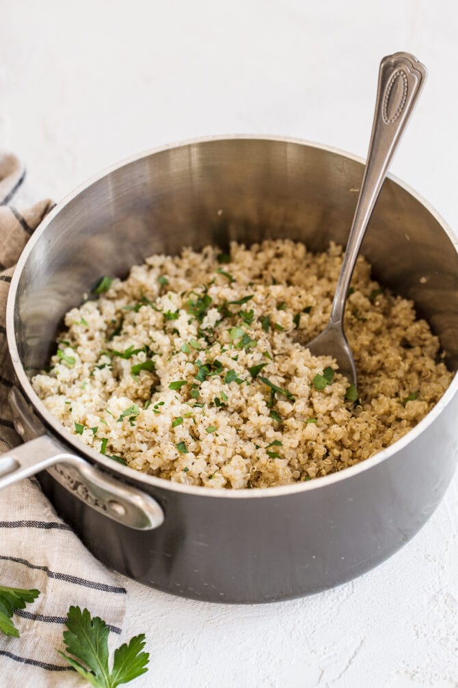Pot of quinoa topped with parsley. A spoon is in the pot.
