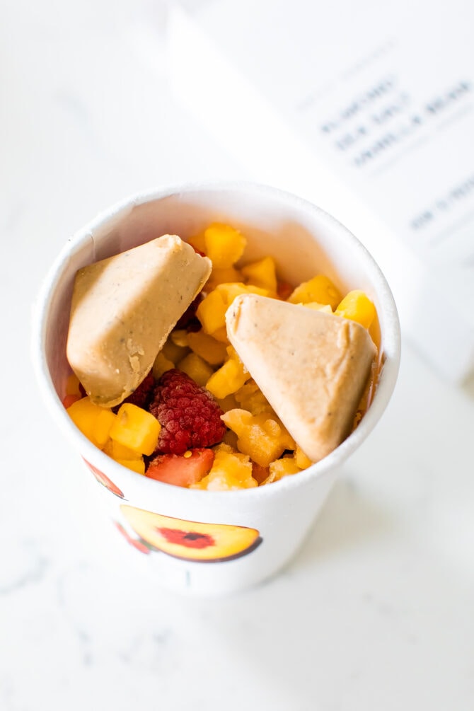 Daily Harvest peach raspberry smoothie cup with two nut mylk wedges on top.