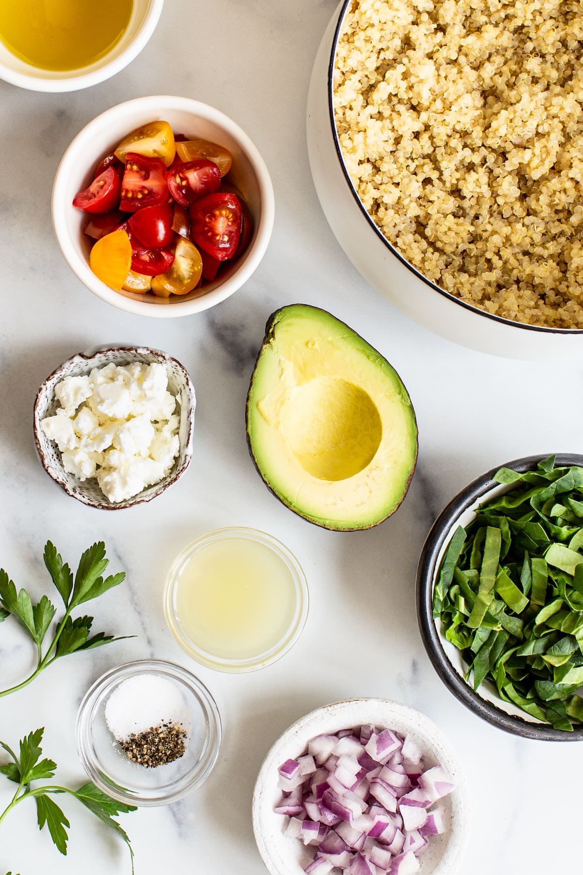 Quinoa, tomatoes, avocado, feta, spinach, lemon juice, spices and red onion measured out in bowls.