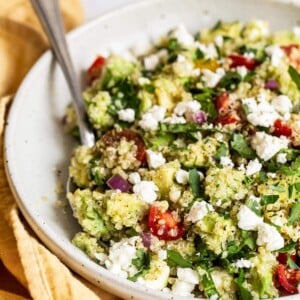 Bowl of quinoa salad with feta, spinach and tomatoes.