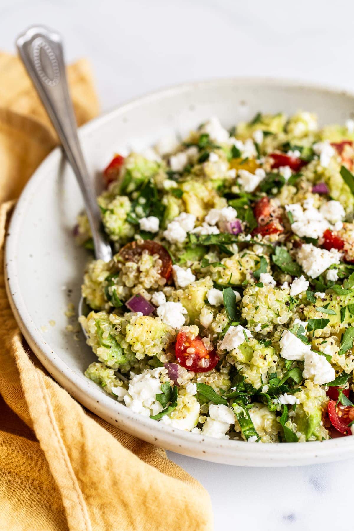 Bowl of quinoa salad with feta, spinach and tomatoes.