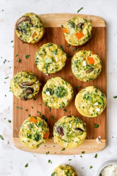 Baked egg and veggie cups on a wood cutting board.