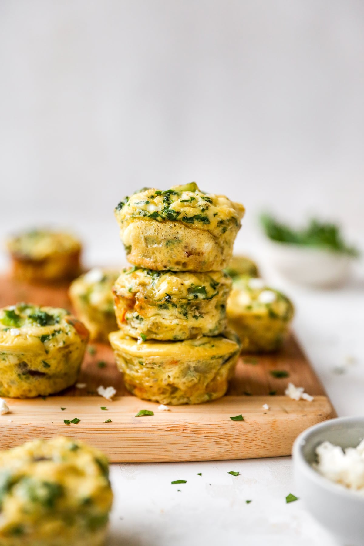 Stack of three egg veggie muffins on a wood cutting board.