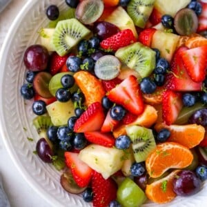 Bowl of fruit salad with strawberries, clementines, kiwi, grapes, blueberries and pineapple. Fruit salad is topped with lime zest.