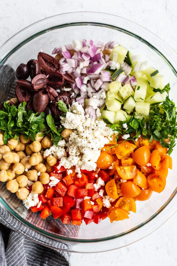 Mixing bowl with kalamata olives, red onion, cucumber, parsley, tomatoes, pepper, chickpeas and feta before being mixed together.