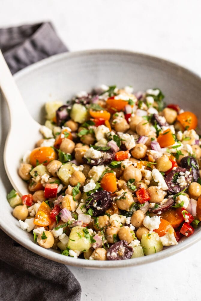Greek chickpea salad in a bowl with a serving spoon.