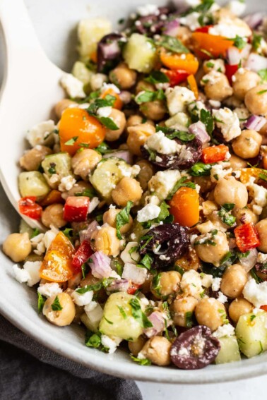 Greek chickpea salad in a bowl with a serving spoon.