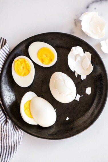 Hard boiled eggs being peeled on a plate.