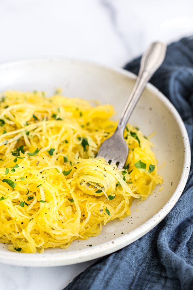 Plate of spaghetti squash topped with parsley. Fork twirling some spaghetti squash.