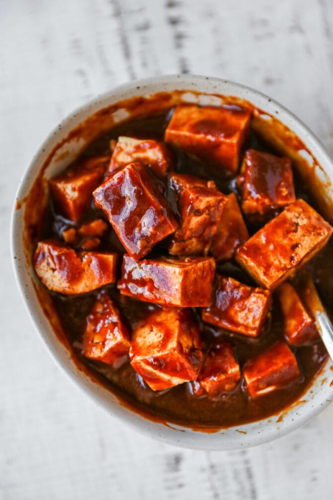 Cubes of tofu in a bowl tossed with kung pao sauce.