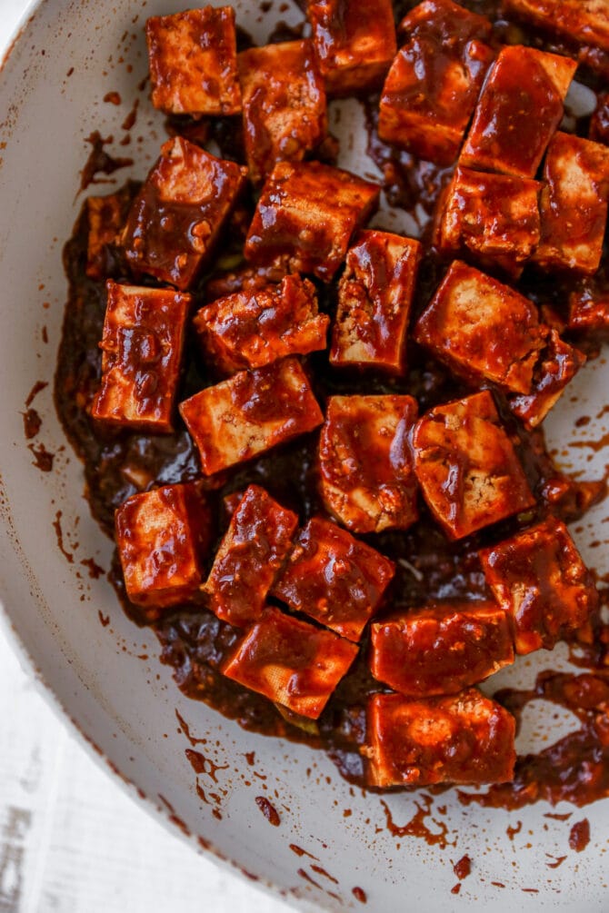 Cubes of tofu being cooked in a pan with kung pao sauce.