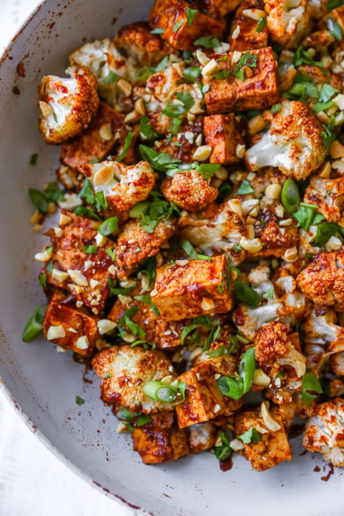 Skillet with kung pao tofu and cauliflower topped with peanuts and green onions.