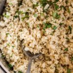 Pot with cooked quinoa topped with chopped parsley and pepper. A spoon is in the pot.