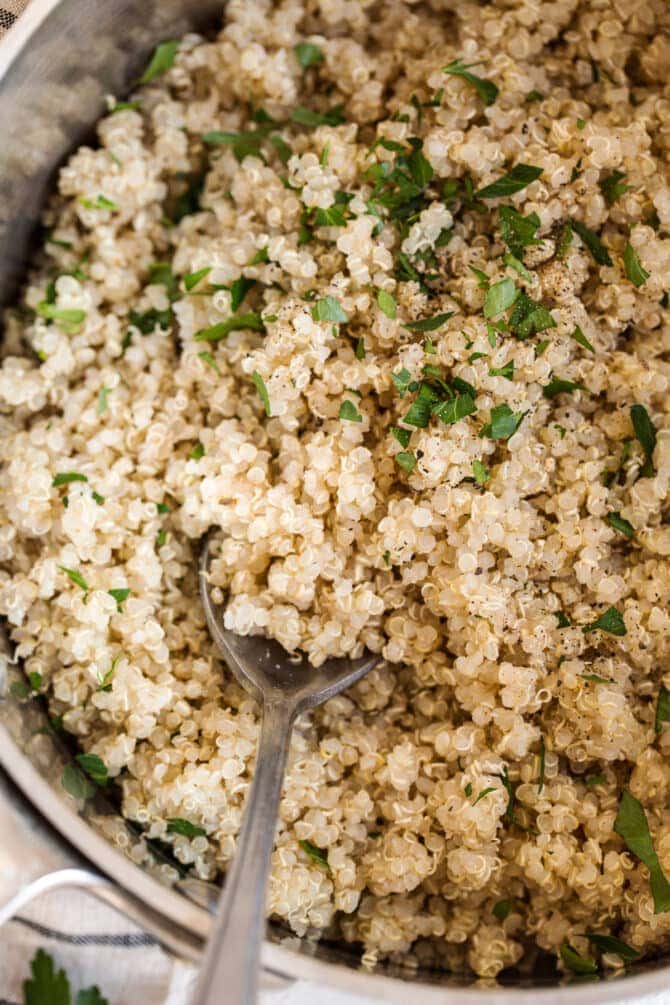 Pot with cooked quinoa topped with chopped parsley and pepper. A spoon is in the pot.