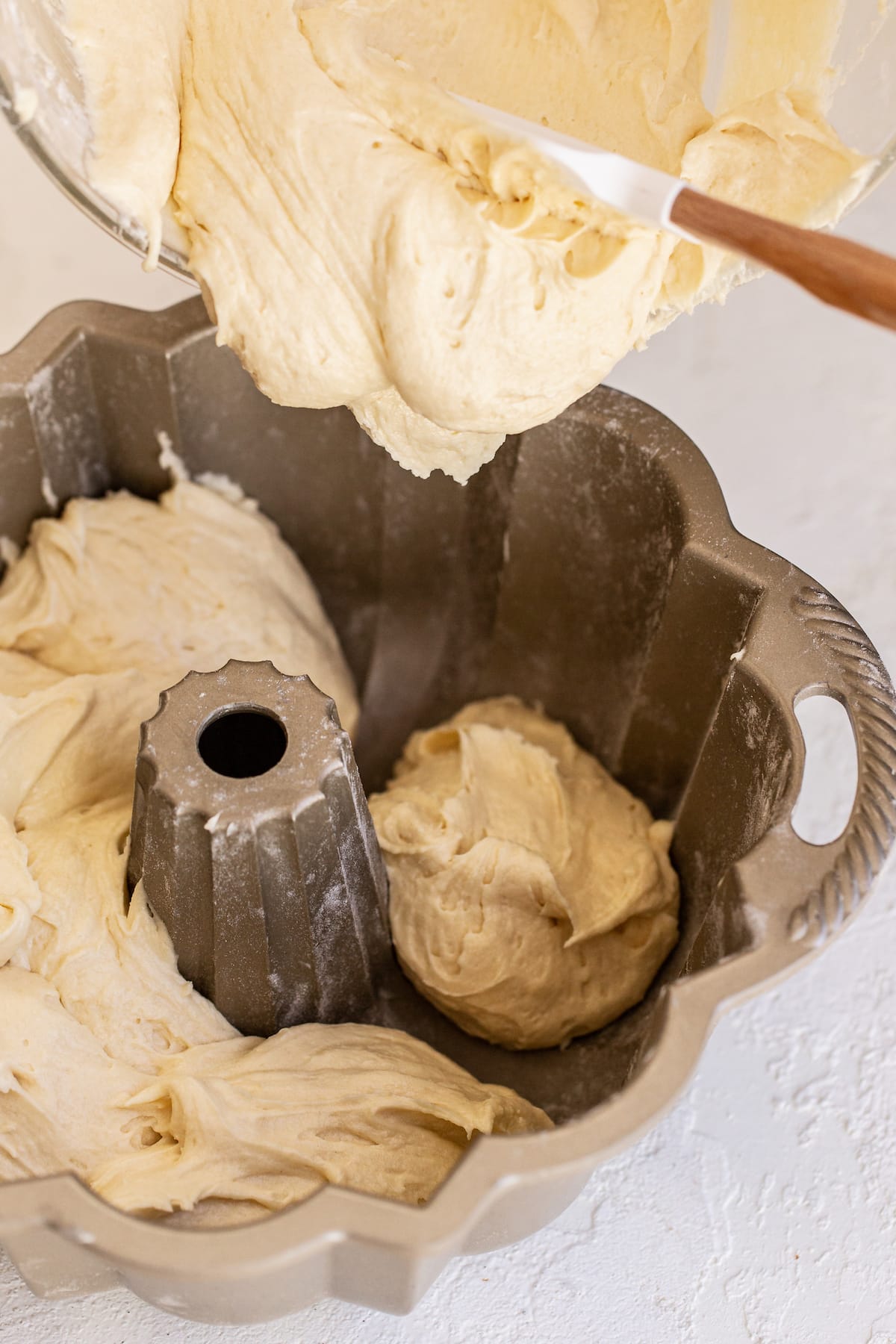 Pouring thick pound cake batter into a bundt pan with a spatula.