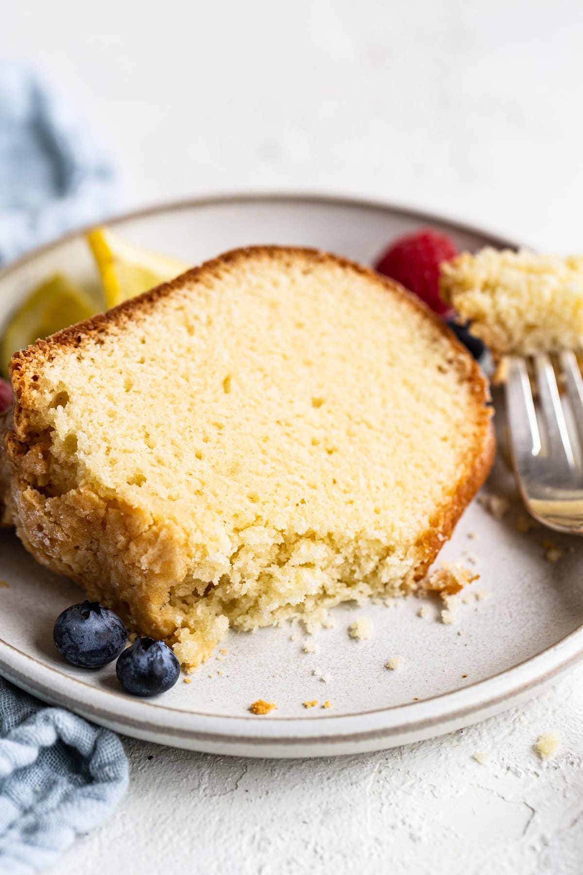 Slice of pound cake on a plate garnished with berries. Fork has taken a bite out of the cake.