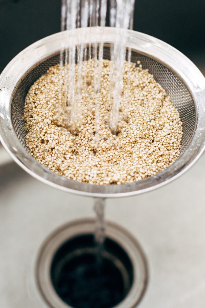 Quinoa in a colander getting rinsed in a sink.